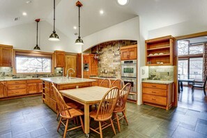 A spacious kitchen with wooden cabinets, a large island, and a dining area with chairs. - Post Oak Estate - Pool, Barn, 2 Guest Homes, 16 Ac (Cleburne)