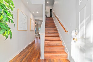 Un escalier en bois mène au deuxième étage, les murs sont blancs et il y a une plante sur la gauche.