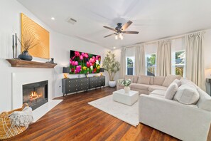 Un salon doté d’une cheminée, d’un grand téléviseur à écran plat, d’un ventilateur de plafond, d’un canapé et d’une table basse.
