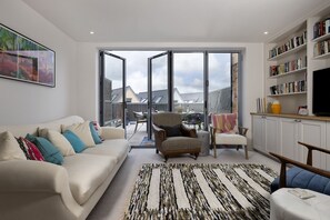 Ein modernes Wohnzimmer mit einer Couch, Sesseln, einem Teppich und einem Bücherregal.