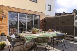 Eine Terrasse im Freien mit Esstisch, Korbstühlen und Blick durch eine Glastür.