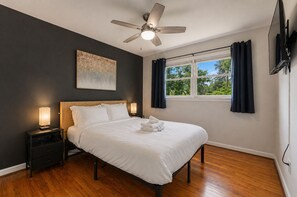 Ein Schlafzimmer mit Bett, Nachttischlampen, Deckenventilator, einem Fenster mit Vorhängen und einem Bild an der Wand.