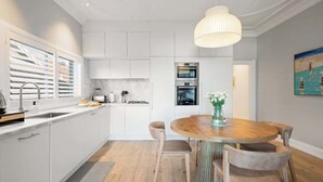Een moderne keuken met witte kastjes, een houten eettafel met stoelen en een hanglamp.