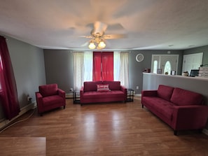 A living room with a ceiling fan, red curtains, a red sofa, and a small table.