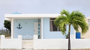 A modern building with a white facade, a metal gate, a palm tree, and a blue barrel.