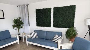 A modern living room with a white sofa, a blue armchair, a coffee table, and a potted plant.