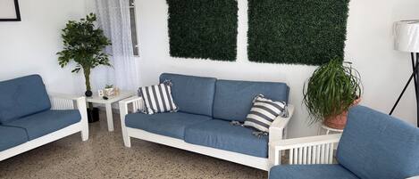 A modern living room with a white sofa, a blue armchair, a coffee table, and a potted plant.