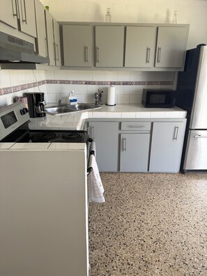 Una cocina con armarios blancos, un refrigerador de acero inoxidable, un microondas, una cafetera y un lavamanos.
