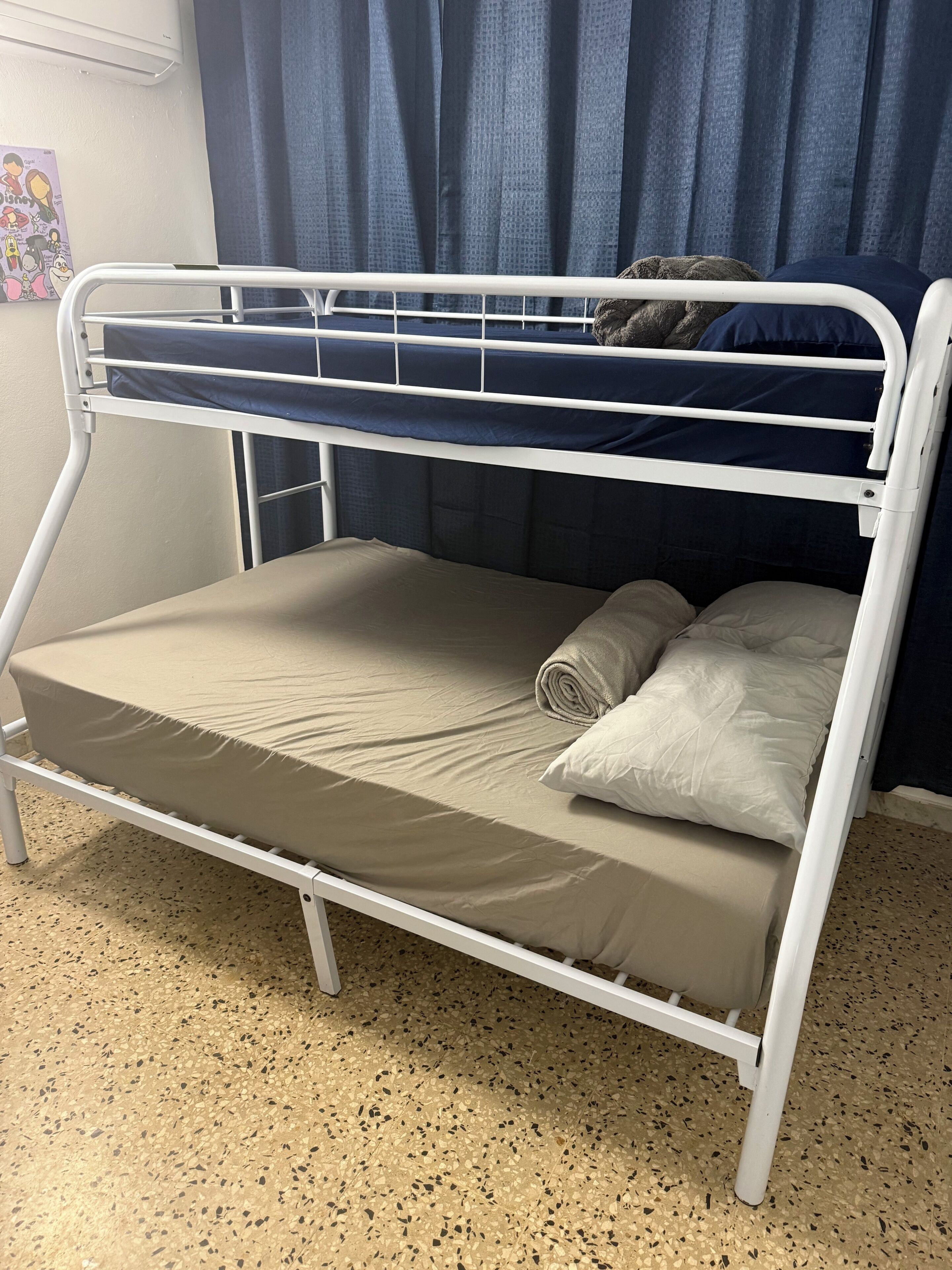 A bunk bed with a mattress and pillows, a wall with a poster, and a window with curtains.