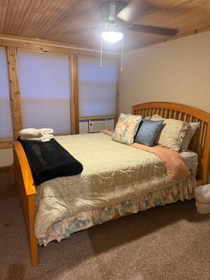 A bedroom with a wooden bed, a ceiling fan, and a window with blinds.