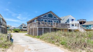 Una propiedad frente a la playa con terraza de madera, zona exterior cubierta y una escalera que conduce a un segundo nivel.