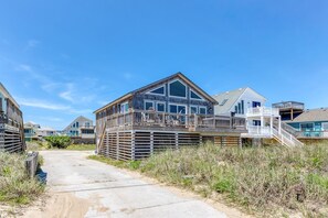 Ein Anwesen direkt am Strand mit einer Holzterrasse, einem überdachten Außenbereich und einer Treppe, die zu einer zweiten Ebene führt.