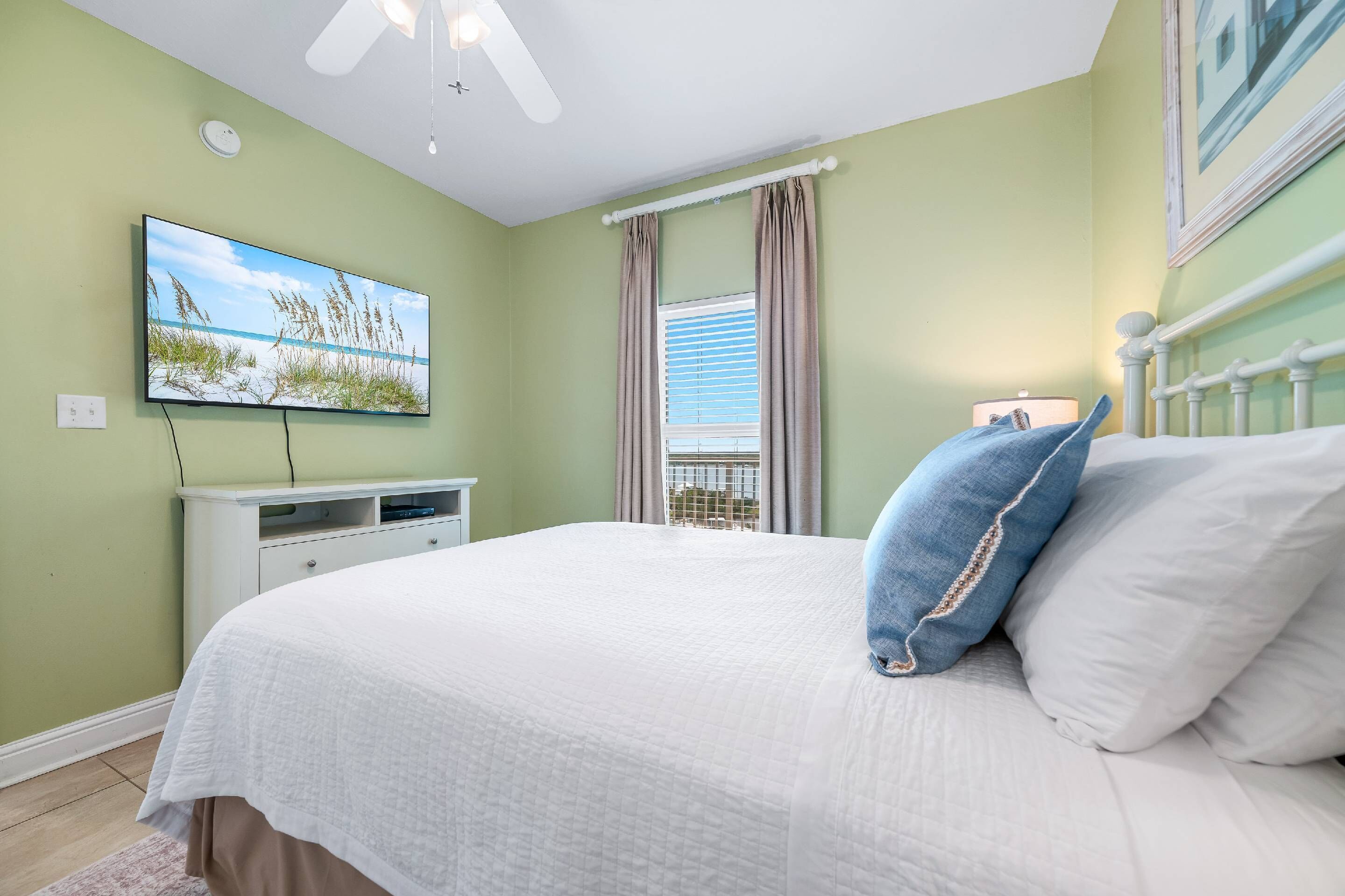 A bedroom with a bed, a television, a window with curtains, and a ceiling fan.