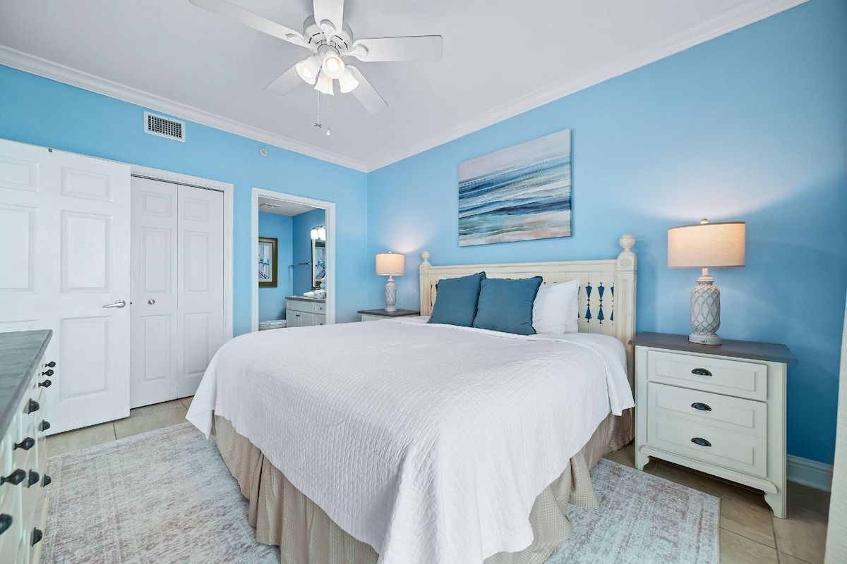 A bedroom with a bed, nightstands, a ceiling fan, and a door.