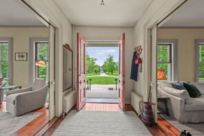 Une pièce spacieuse avec une grande ouverture donnant sur un jardin, un canapé, un fauteuil et une table avec une lampe.