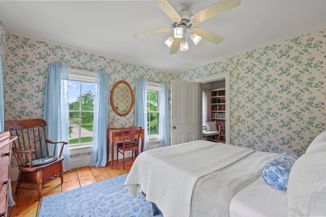 A bedroom with a bed, a desk, a chair, a ceiling fan, and a bookshelf.