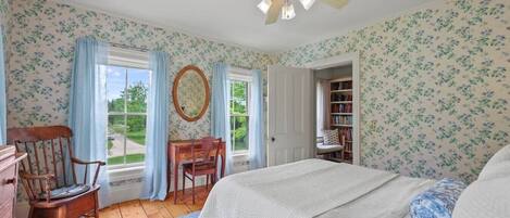 A bedroom with a bed, a desk, a chair, a ceiling fan, and a bookshelf.