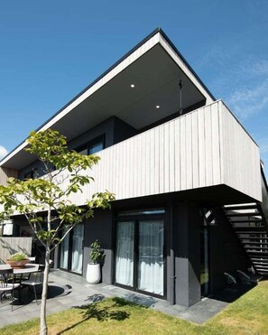 A modern two-story house with a flat roof, large windows, and a small outdoor seating area with a table and chairs. - Urban Art House - Modern City Retreat with Spa Pool (Nelson)