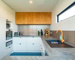 A modern kitchen with white cabinetry, a wooden upper cabinet, a microwave, a toaster, and a sink with a unique faucet. - Urban Art House - Modern City Retreat with Spa Pool (Nelson)