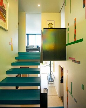 A staircase with teal steps leading to a room with a window, a framed picture on the wall, and a door at the bottom. - Urban Art House - Modern City Retreat with Spa Pool (Nelson)