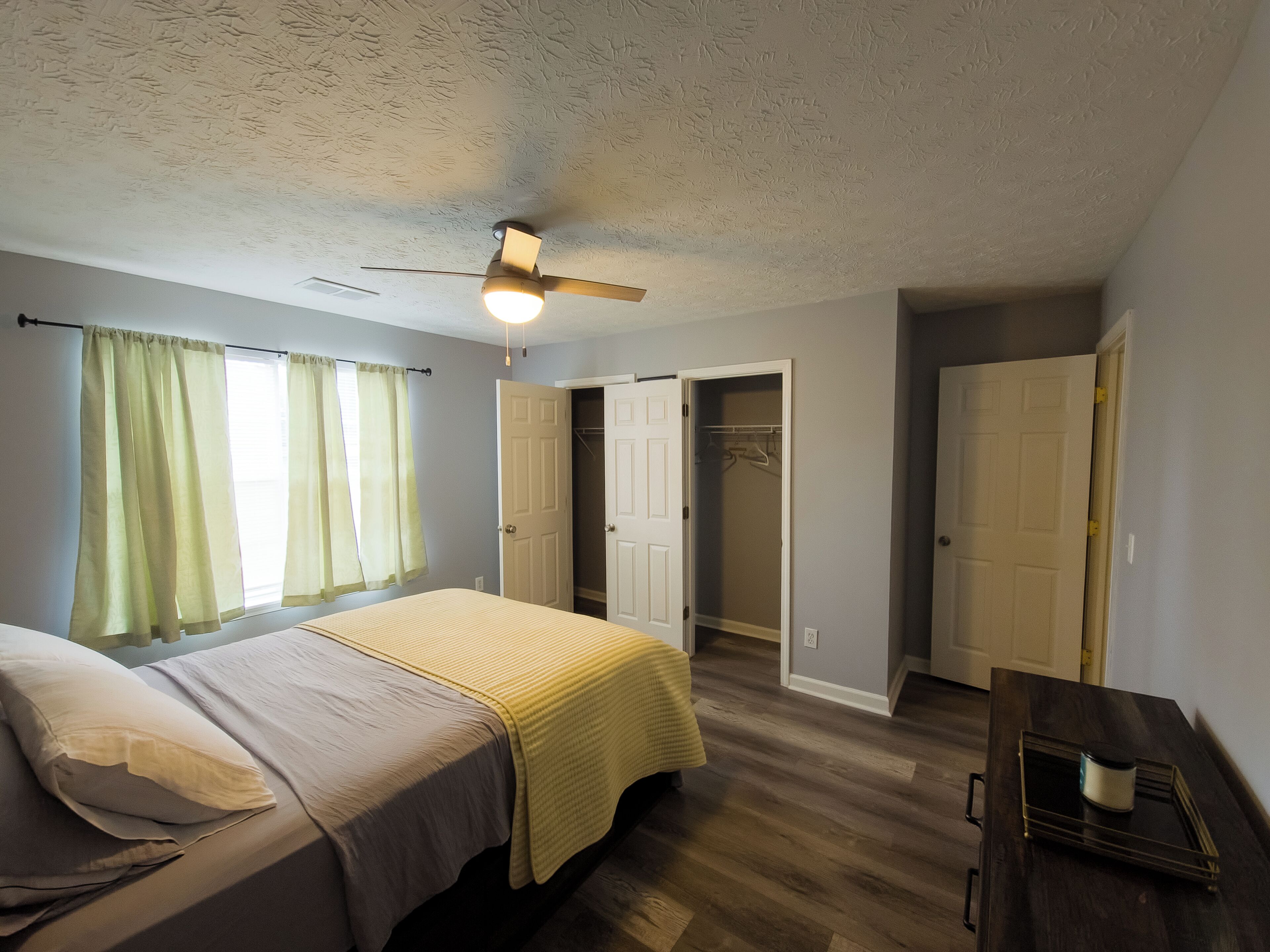 A bedroom with a bed, a ceiling fan, a walk-in closet, and a dresser.