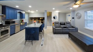 A modern kitchen with blue cabinets, a dining area with bar stools, a gray sofa, and a ceiling fan. - Beautiful 3-bedroom Serenity house in a Cul-de-Sac with AC in charming Decatur (Decatur)