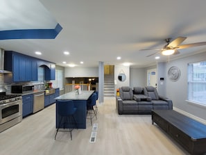 A modern kitchen with blue cabinets, a dining area with bar stools, a gray sofa, and a ceiling fan. - Beautiful 3-bedroom Serenity house in a Cul-de-Sac with AC in charming Decatur (Decatur)