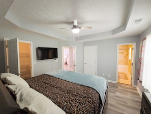 A bedroom with a bed, a ceiling fan, a TV, and a door leading to another room. - Beautiful 3-bedroom Serenity house in a Cul-de-Sac with AC in charming Decatur (Decatur)