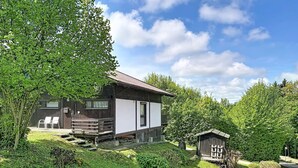 Een rustieke blokhut met houten gevel, een balkon en een kleine schuur, gelegen in een weelderig groene omgeving.