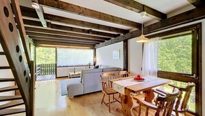 Een houten interieur met een eettafel, stoelen, een bank en een trap.