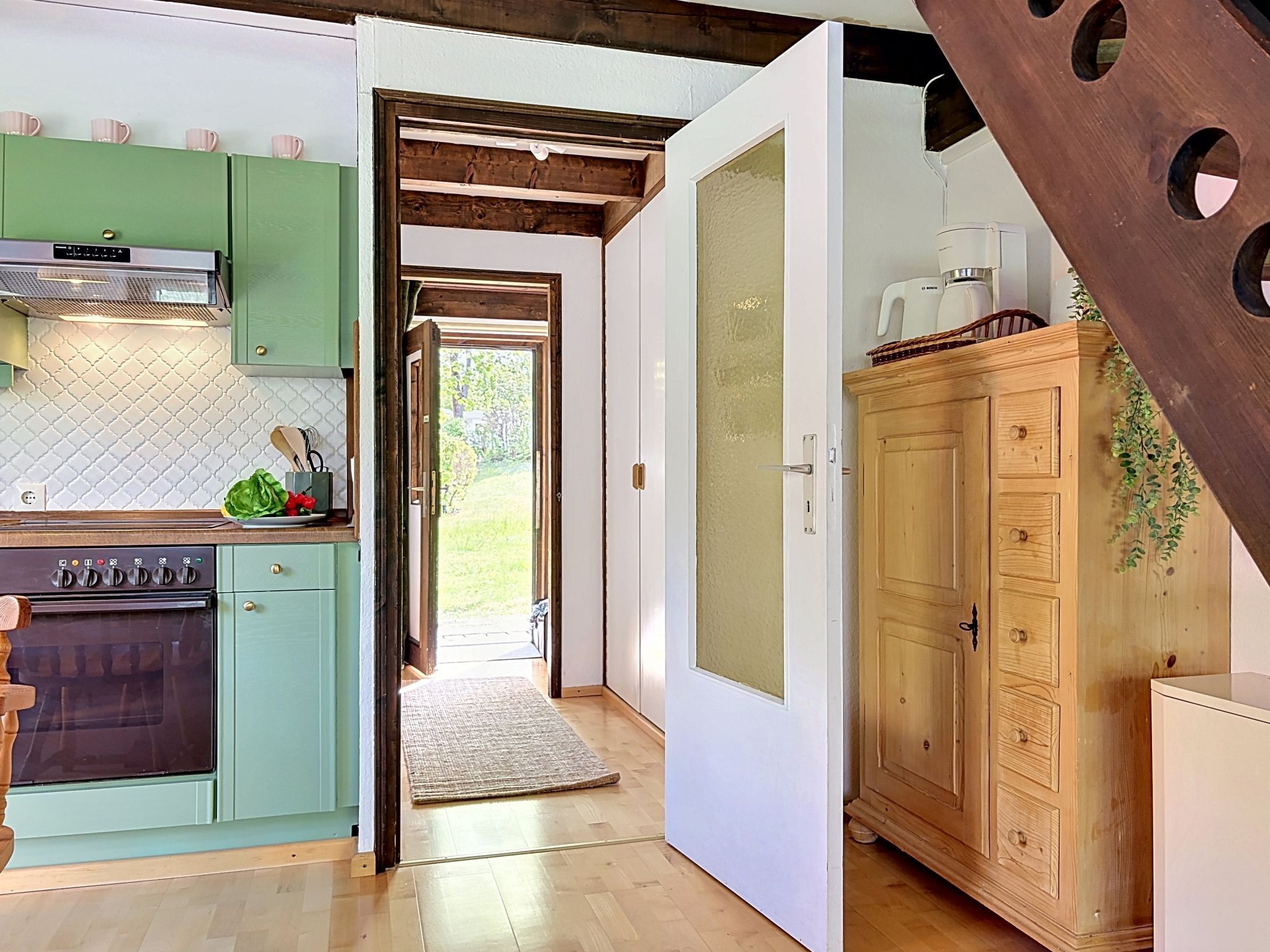 A kitchen with green cabinets, a stove, and a wooden cabinet with a plant.