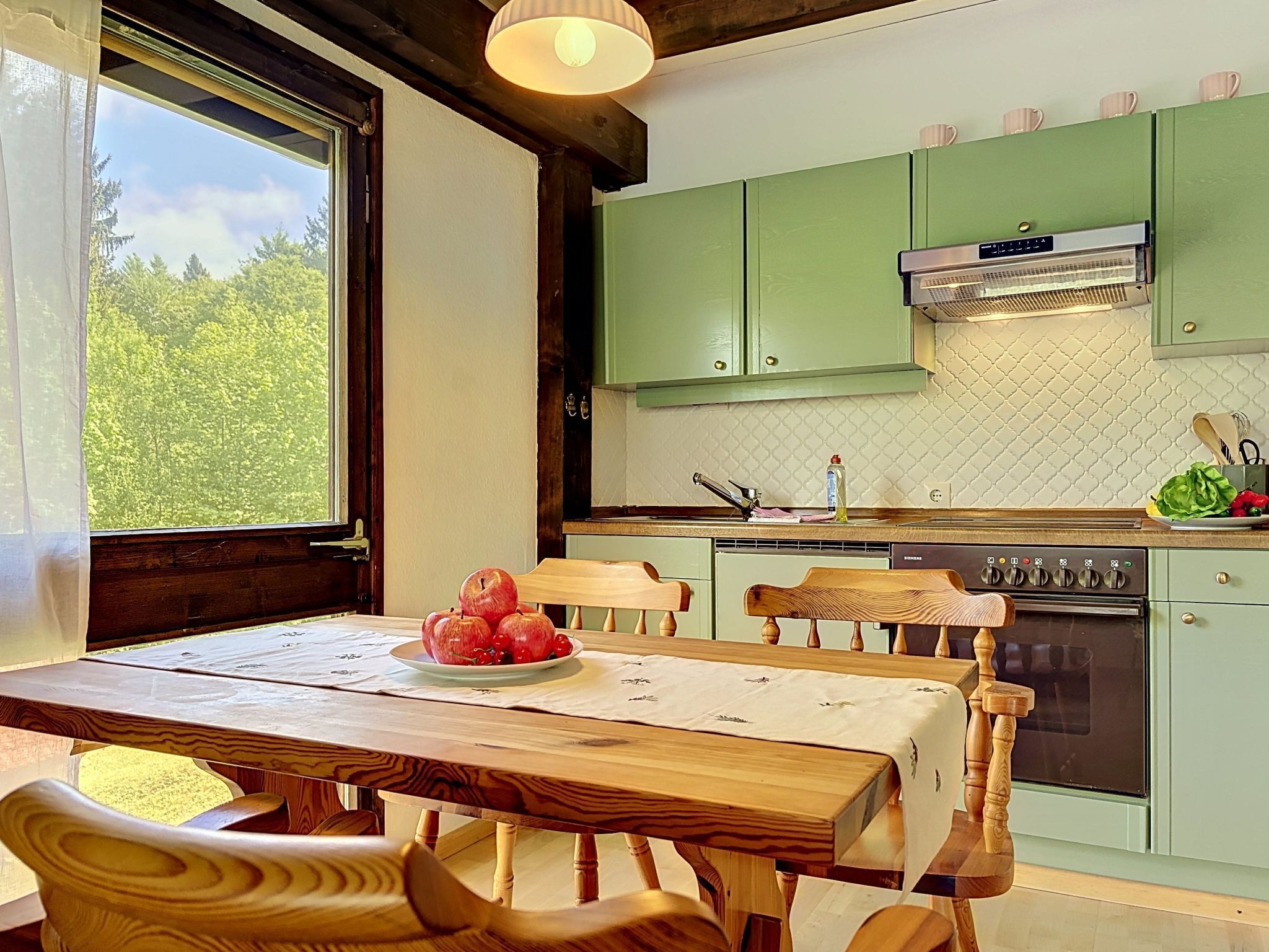 Une cuisine avec des meubles en bois, un fourneau et une fenêtre donnant sur les arbres.