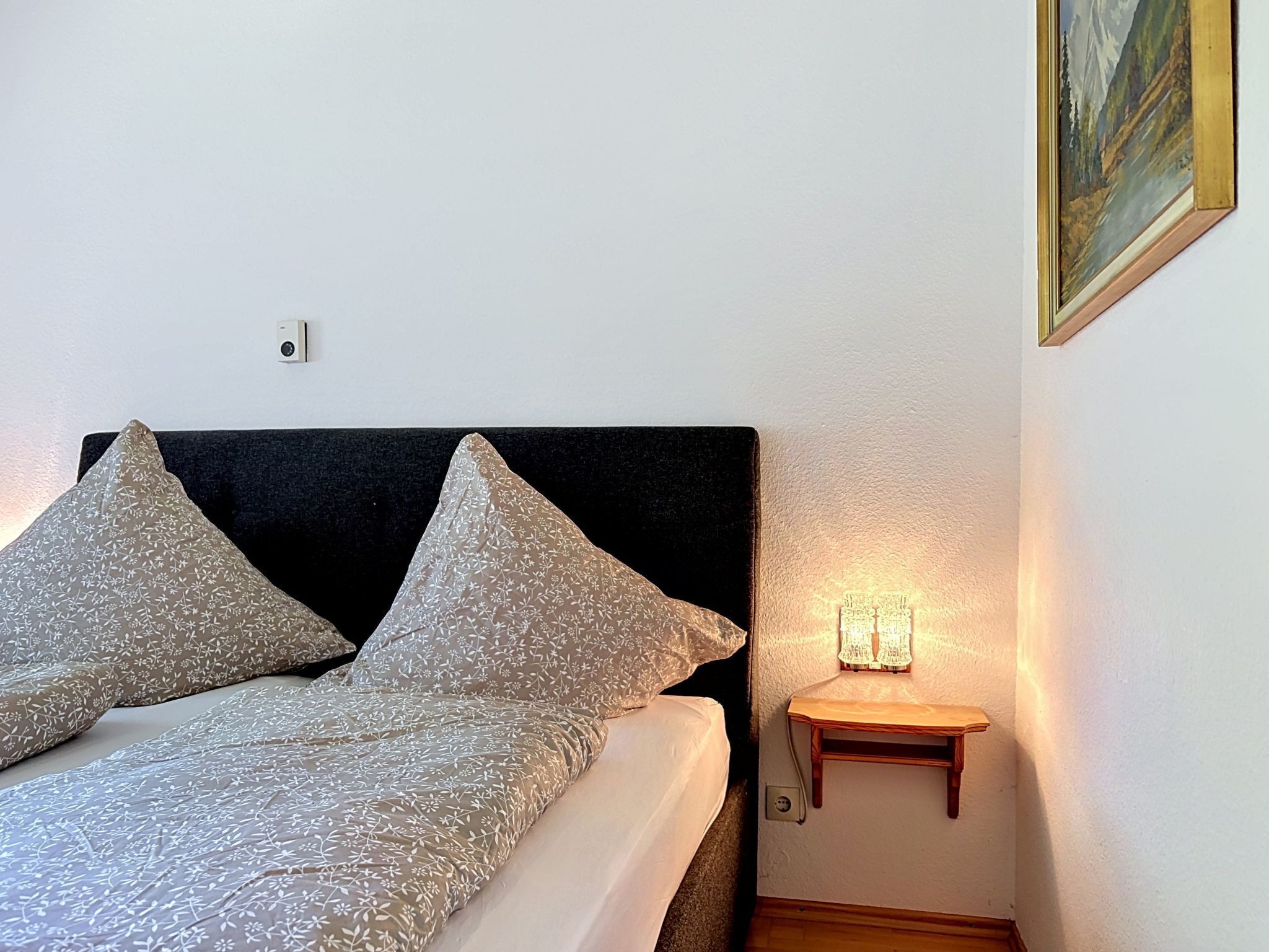 Un lit avec une literie à motifs, une table de chevet avec une lampe et un tableau accroché au mur.
