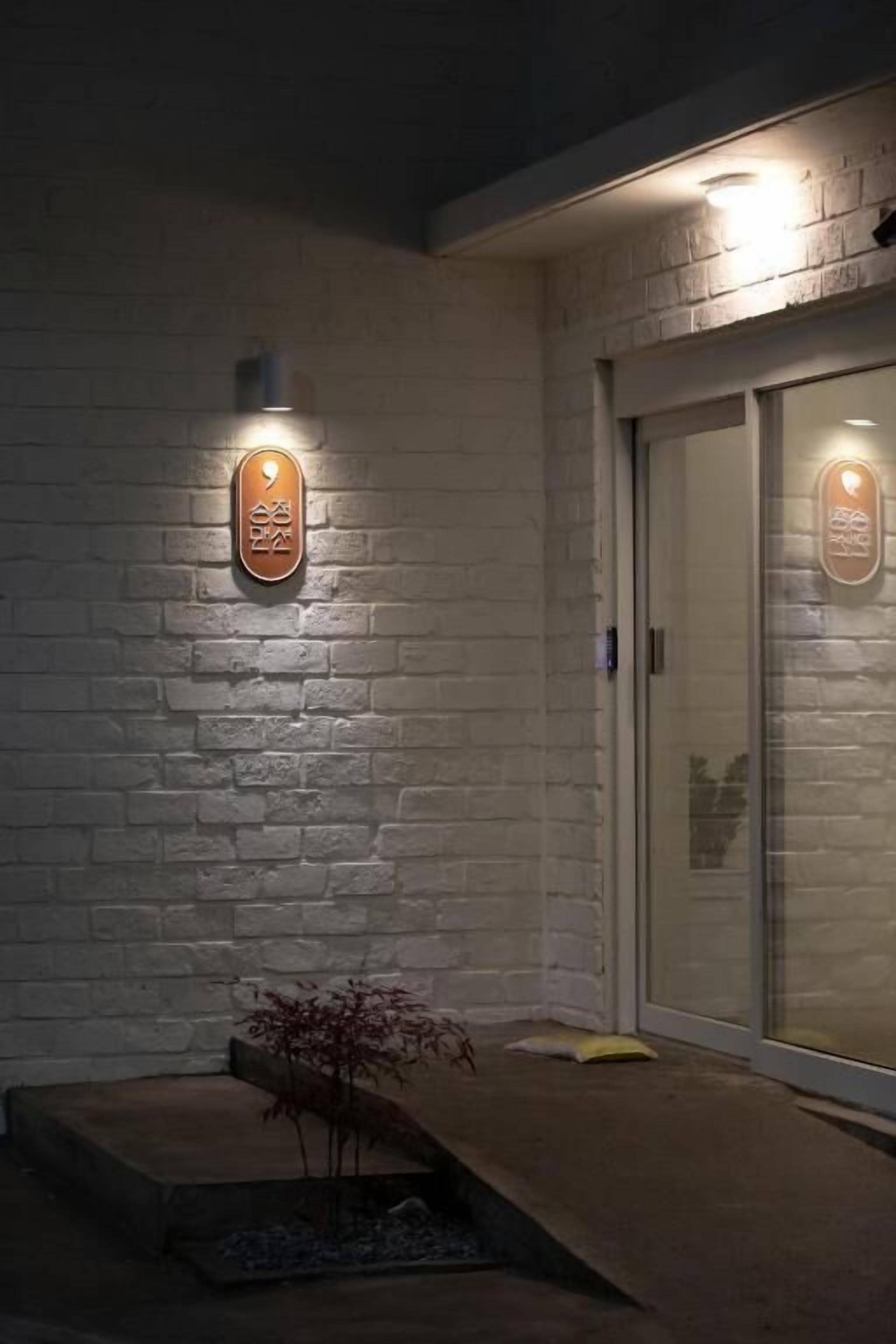 Fachada de un edificio con pared de ladrillo blanco, puerta de vidrio y dos letreros iluminados.