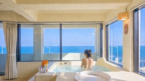 A room with a large window, a hot tub, and a view of the sea.