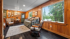 A cozy room with a bed, a wooden chair, a table, and a large window with a forest view.