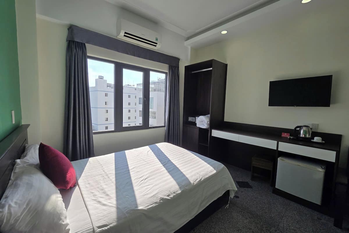 A hotel room with a bed, a desk, a television, and a window with curtains.