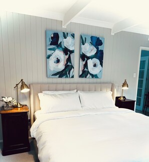 Een slaapkamer met een bed, twee nachtkastjes, een wandlamp en twee bloemschilderijen.
