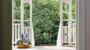 Une terrasse en bois avec un panier rempli d’objets et une porte blanche donnant sur un jardin luxuriant.