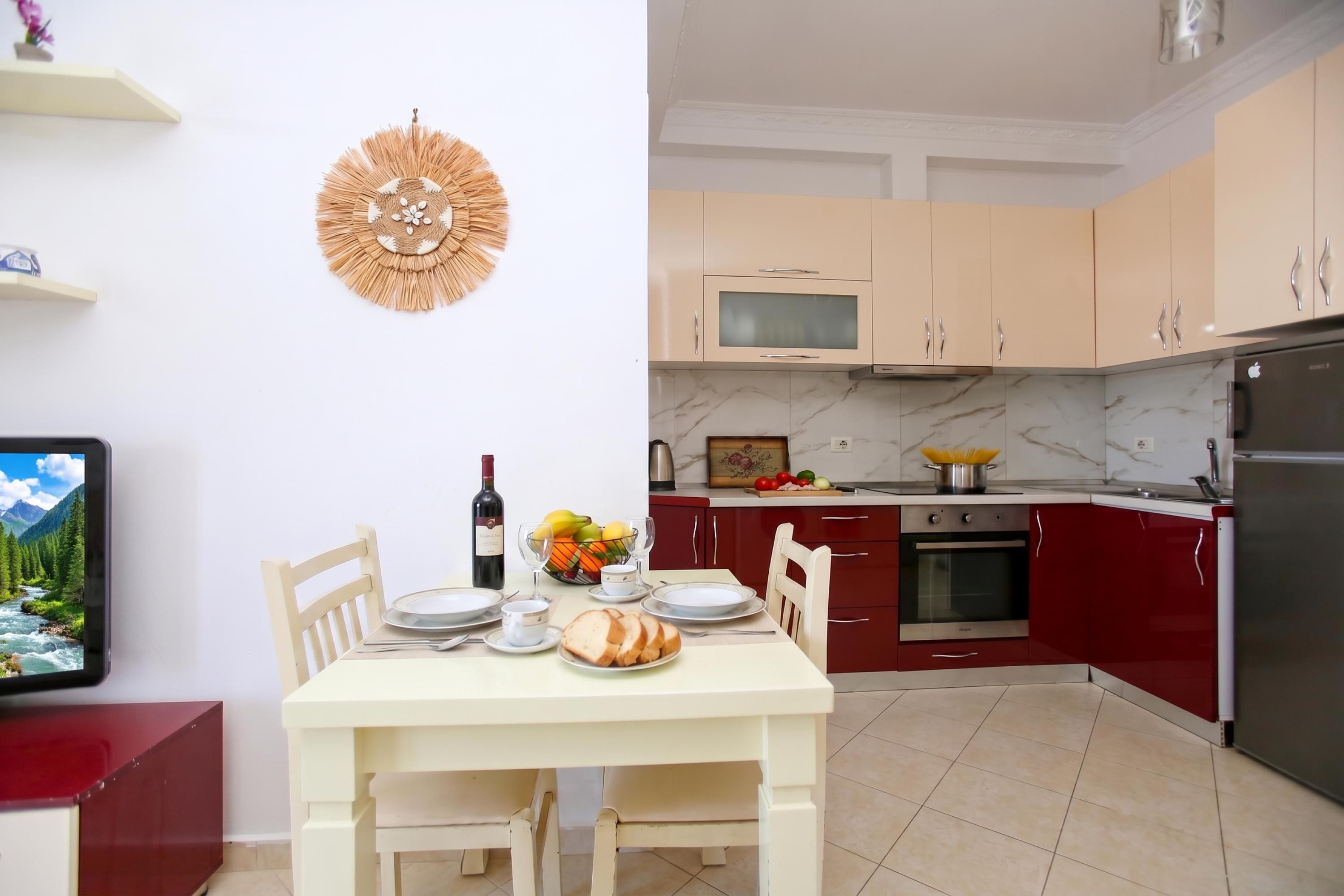 Une cuisine moderne avec un coin repas, équipée d’un réfrigérateur, d’un four, d’un micro-ondes et d’une table à manger, cette dernière étant dressée avec des assiettes, une bouteille de vin et un panier de fruits.