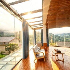 Una habitación moderna con piso de madera, un sofá, una mesa y ventanas amplias que ofrecen vistas a un paisaje montañoso.