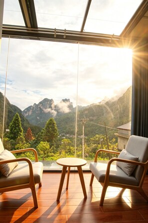 Una habitación con un gran ventanal que ofrece vistas a un paisaje montañoso, dos sillas y una pequeña mesa redonda.