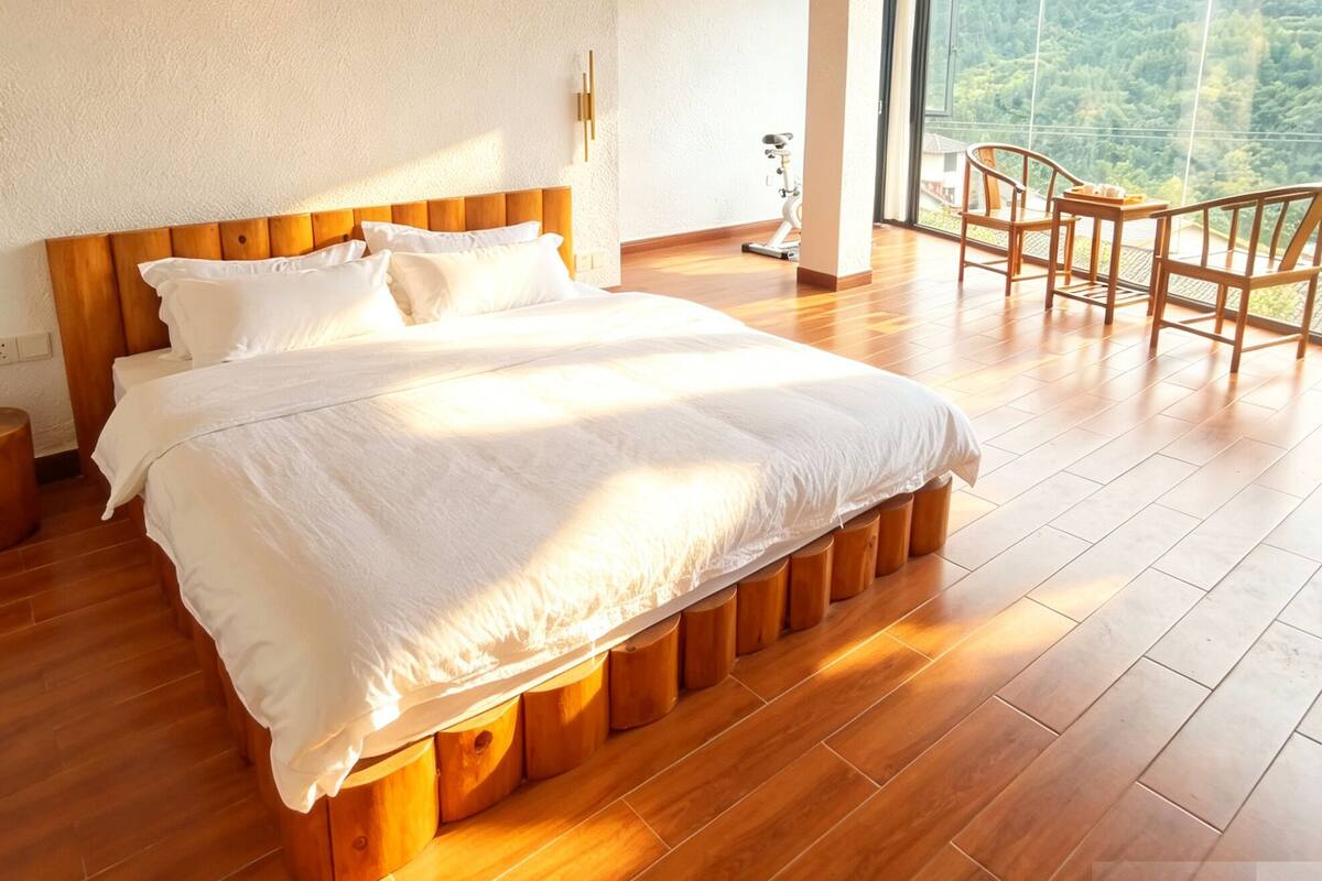 A bedroom with a large bed, wooden flooring, a wooden ceiling, a window with a mountain view, and a small table with chairs.