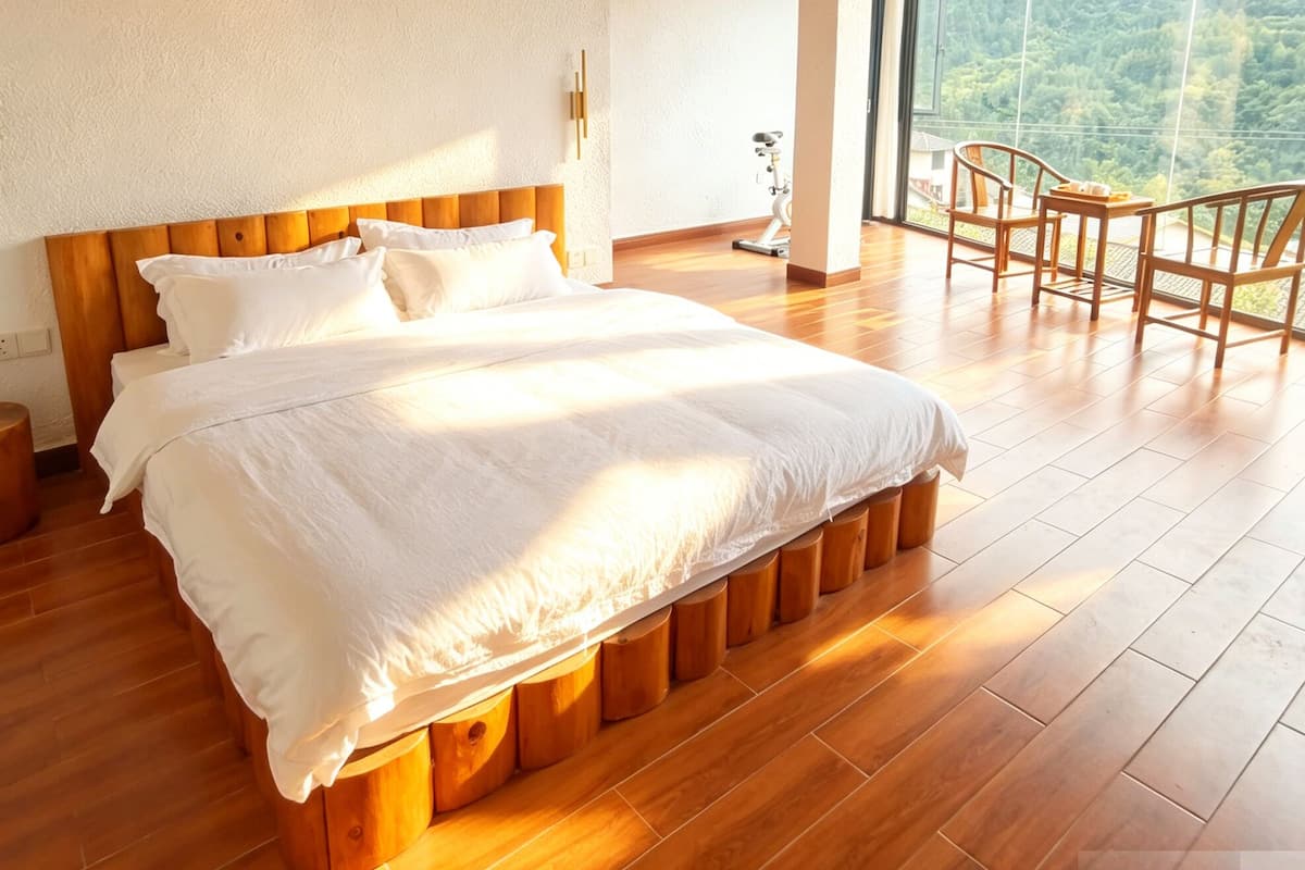 A bedroom with a large bed, wooden flooring, a wooden ceiling, a window with a mountain view, and a small table with chairs.