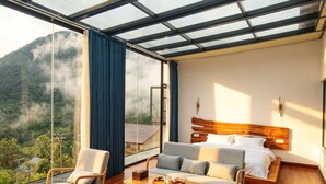Ett modernt hotellrum med ett stort glastak, ett trägolv, en säng med ett trägavelt, en soffa, en fåtölj och ett litet bord.