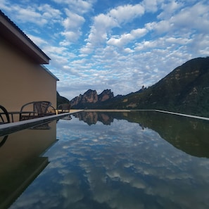 Una vista despejada de una cordillera reflejada en un cuerpo de agua tranquilo, un edificio de techo plano y una silla al borde del agua.