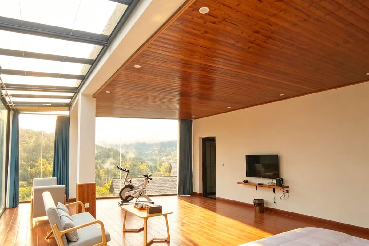 A spacious bedroom with a large bed, a TV mounted on the wall, and a view of the outdoors through a large window.