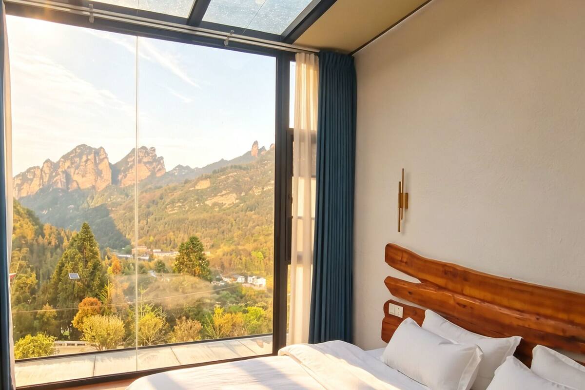 A bedroom with a large skylight, a wooden headboard, and a view of mountains.