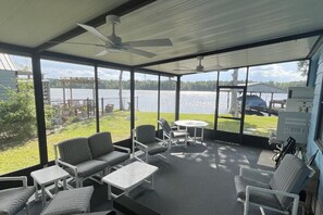 A covered outdoor area with seating, a fan, and a view of a lake.