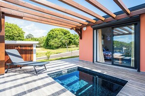 Ein moderner Poolbereich im Freien mit einer Holzpergola, einer Liege und einer Glastür zu einem Raum.